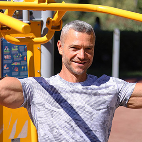 Natural Pharmaceuticals ProMan Plus Vidutinio amžiaus vyras sportuoja lauko treniruoklių aikštelėje saulėtą dieną.